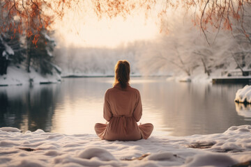 A woman sitting on the snow-covered ground looking at a lake. Perfect for winter-themed designs, outdoor activities, mindfulness, nature appreciation, and peaceful scenery concepts. - obrazy, fototapety, plakaty