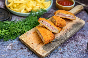  Crispy  deep fried home made     chicken Cordon bleu with cheese   and ham  and french fries on wooden rustic background.   - obrazy, fototapety, plakaty