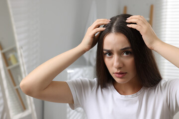 Emotional woman examining her hair and scalp at home. Dandruff problem