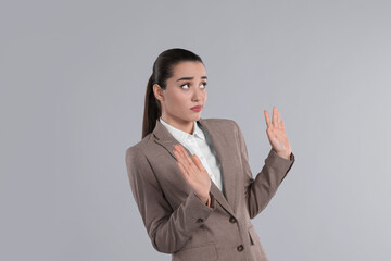 Young woman in suit avoiding something on light grey background