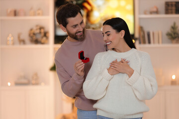 Making proposal. Man with engagement ring surprising his girlfriend at home on Christmas