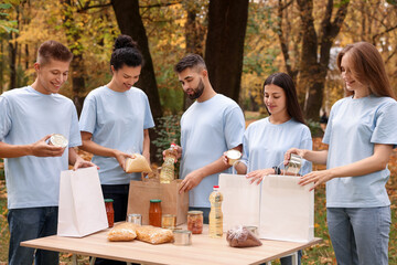 Group of volunteers packing food products at table in park