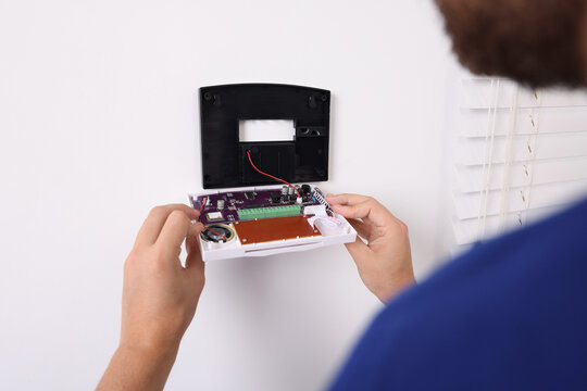 Man installing home security alarm system on white wall indoors, closeup