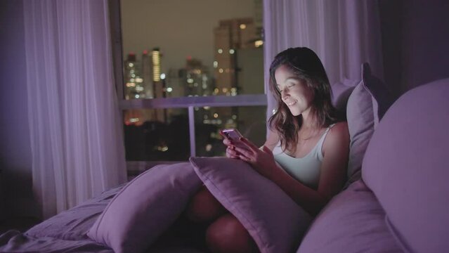 A relaxed woman using smartphone device at home living room couch at night. Closeup woman staring at phone at night
