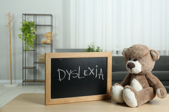 Teddy bear and small blackboard with word Dyslexia on wooden table indoors