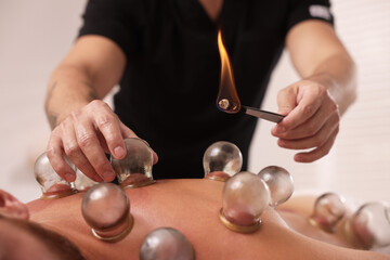 Therapist giving fire cupping treatment to patient indoors, closeup