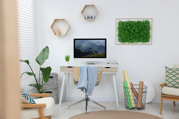 Green artificial plant wall panel and desk with computer in light room. Interior design