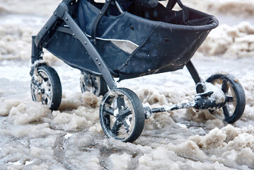 Baby stroller stuck on wet snow in winter season. Baby carriage stand on snowy icy road after heavy...