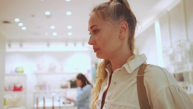 Close-up profile portrait attractive woman at fashion accessory boutique. Caucasian blonde woman in shopping mall looking at some trendy handbags