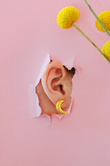 Female ear close-up on a pink background with flowers. Copy space. Torn paper background. The...