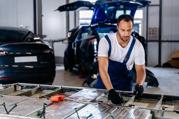 Arabian male technician engages with an EV Car Battery Cell Module troubleshooting a modern electric vehicle battery removed from the vehicle. Mechanic examining a car engine with voltmeter.