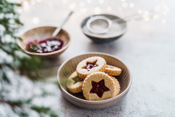 Weihnachtskekse mit Erdbeerkonfitüre in einer Schüssel und Koniferen. Grauer Tisch, Lichter.