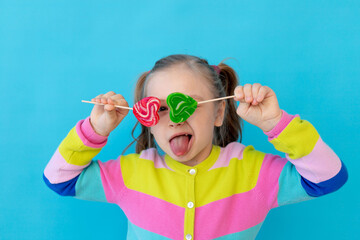 portrait of a cute little girl with lollipops in a striped jacket covering her eyes with them, a...