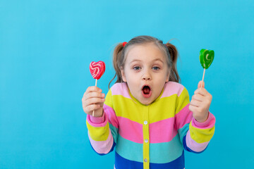 portrait of a surprised little girl with lollipops in a striped jacket, a large candy on a stick....
