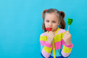 portrait of a cute little girl with lollipops in a striped jacket. the child eats and licks a large...