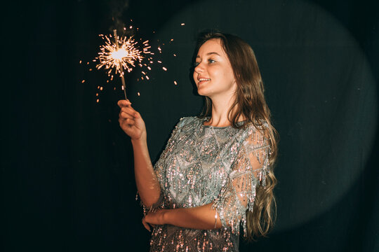 Smiling woman looking at sparkler in front of black curtain