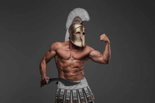 Portrait of an ancient Greek hoplite, posing in a studio with a bare muscular torso, wearing a helmet, and holding a gladius, set against a gray background