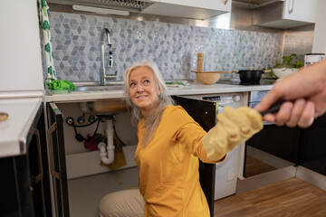 Mature woman doing plumbing in kitchen at home
