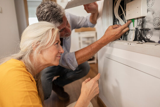 Woman assisting man examining fusebox at home