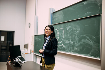 Smiling businesswoman standing in front of greenboard at auditorium