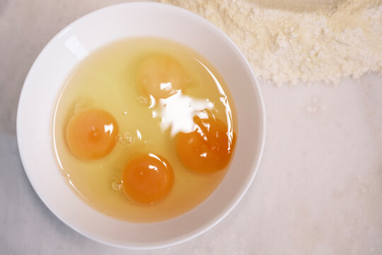 Isolated raw chicken eggs, top view of four raw egg in white bowl on white marble.