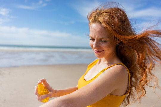 Smiling woman spraying suntan lotion on hand at beach