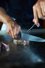 Professional chef cooking delicious juicy beef steak on restaurant stove, selective focus