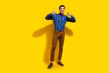 Full size photo of satisfied optimistic guy dressed striped shirt brown trousers showing thumbs up isolated on yellow color background
