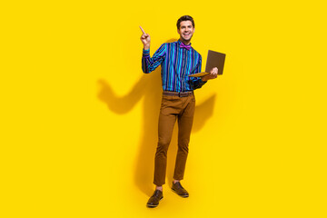 Full size photo of good mood guy dressed striped shirt hold laptop indicating at discount empty space isolated on yellow color background