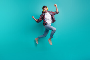 Fototapeta na wymiar Full length photo of good mood lucky guy wear checkered shirt jumping high rising fists listening songs isolated teal color background