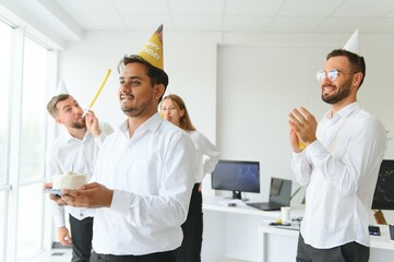 happy business team with birthday cake and gifts greeting indian male colleague at office party