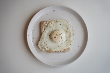 Close up of a fried eggs in a white plate at the kitchen table.
