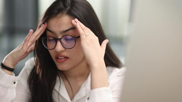 Young businesswoman expressing misunderstanding or tiredness while sitting by desk in front of laptop and looking through online data