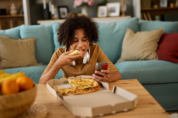 Teenage boy using phone while having pizza at home