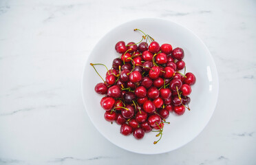 Fresh red cherries fruit on a white plate on a white surface