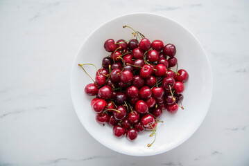 Fresh red cherries fruit on a white plate on a white surface