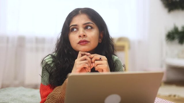 Portrait of pretty creative indian woman student thinks questioningly about difficult choice choose imagine plan in mind has doubts create idea laying on bed at home