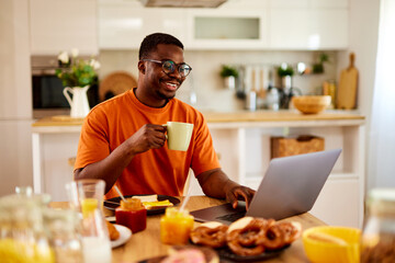 Fototapeta na wymiar African American man using laptop while enjoying breakfast at home