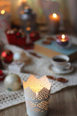 Various colorful Christmas decorations, soft blanket, cup of tea, sweet snacks and lit candles on the table. Cozy Christmas atmosphere at home. Selective focus.