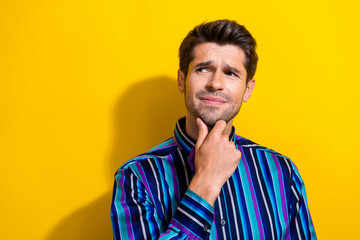 Photo of suspicious gloomy man dressed striped shirt hold finger on chin look empty space isolated on vivid yellow color background