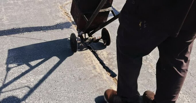 Patcher performs work that involves coating asphalt cracks, sealing them, applying bitumen emulsion to roads.