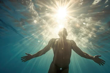 Fotobehang Man swimming from the transparent depths of the sea towards the radiance of sunlight. Vacation, active rest, relaxation. © BetterPhoto