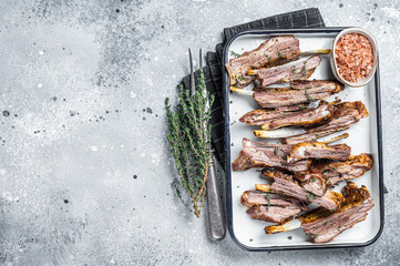 BBQ smoked lamb ribs, mutton spareribs, sliced meat in steel tray with herbs. Gray background. Top...