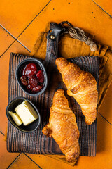 Delicious breakfast with fresh croissants served with butter and jam. Orange background. Top view