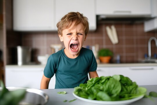Junge mag keinen Spinat essen. Kind ekelt sich vor Spinat und weigert sich zu essen, mit ver&auml;rgertem Gesichtsausdruck.. 