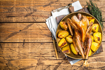 Roasted guinea fowl with herbs and potato, cooked farm eco bird. Wooden background. Top view. Copy...