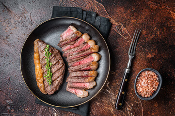 Sliced grilled medium rare Top sirloin beef steak on a plate. Dark background. Top view