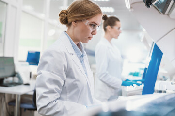 A team of laboratory technicians conduct a series of tests on a chemical analyzer in a biological laboratory. Two female scientists work in a modern equipped computer laboratory
