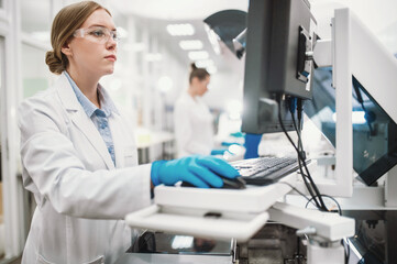 A team of laboratory technicians conduct a series of tests on a chemical analyzer in a biological laboratory. Two female scientists work in a modern equipped computer laboratory - obrazy, fototapety, plakaty