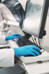 laboratory technician in lab coat and gloves performs series of tests  in bio laboratory. Doctor takes tests on chemical analyzer, closeup without face. Working at  computer in modern laboratory